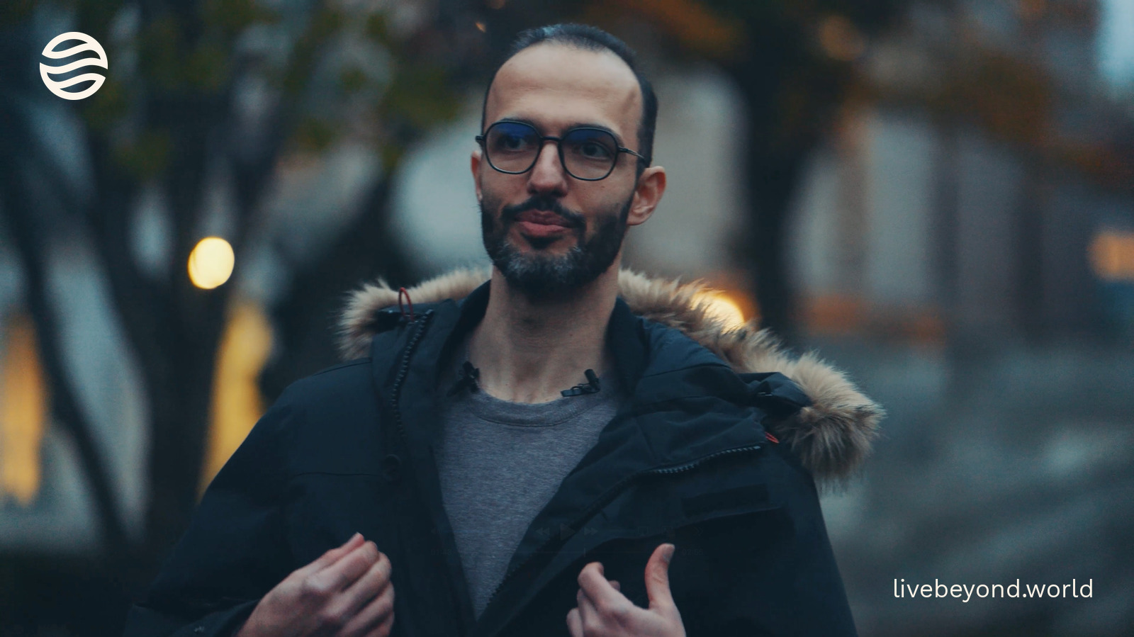 Mahdi Moqri in a dark jacket, explaining with both hands, outdoors at dusk.