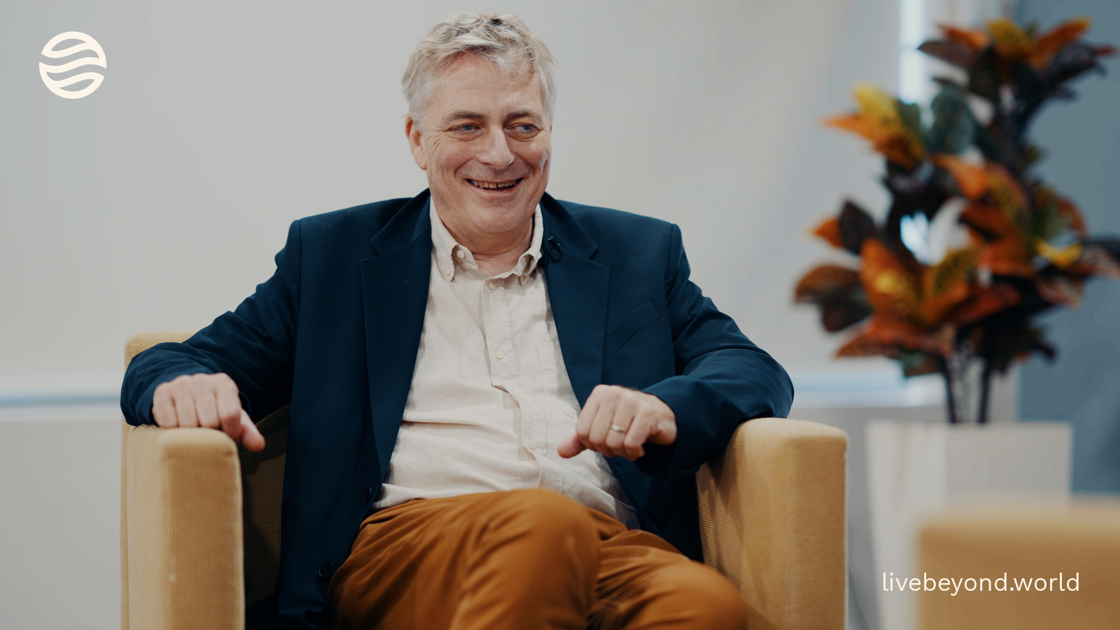 Guido Kroemer laughing in an armchair, a plant beside him.