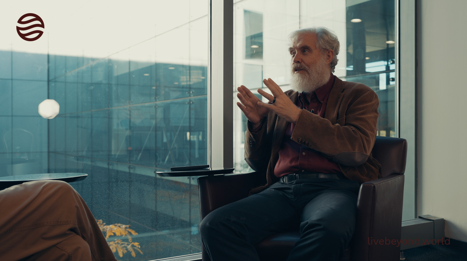George Church talking with his hands, sitting in a leather armchair by a tall window at Harvard.