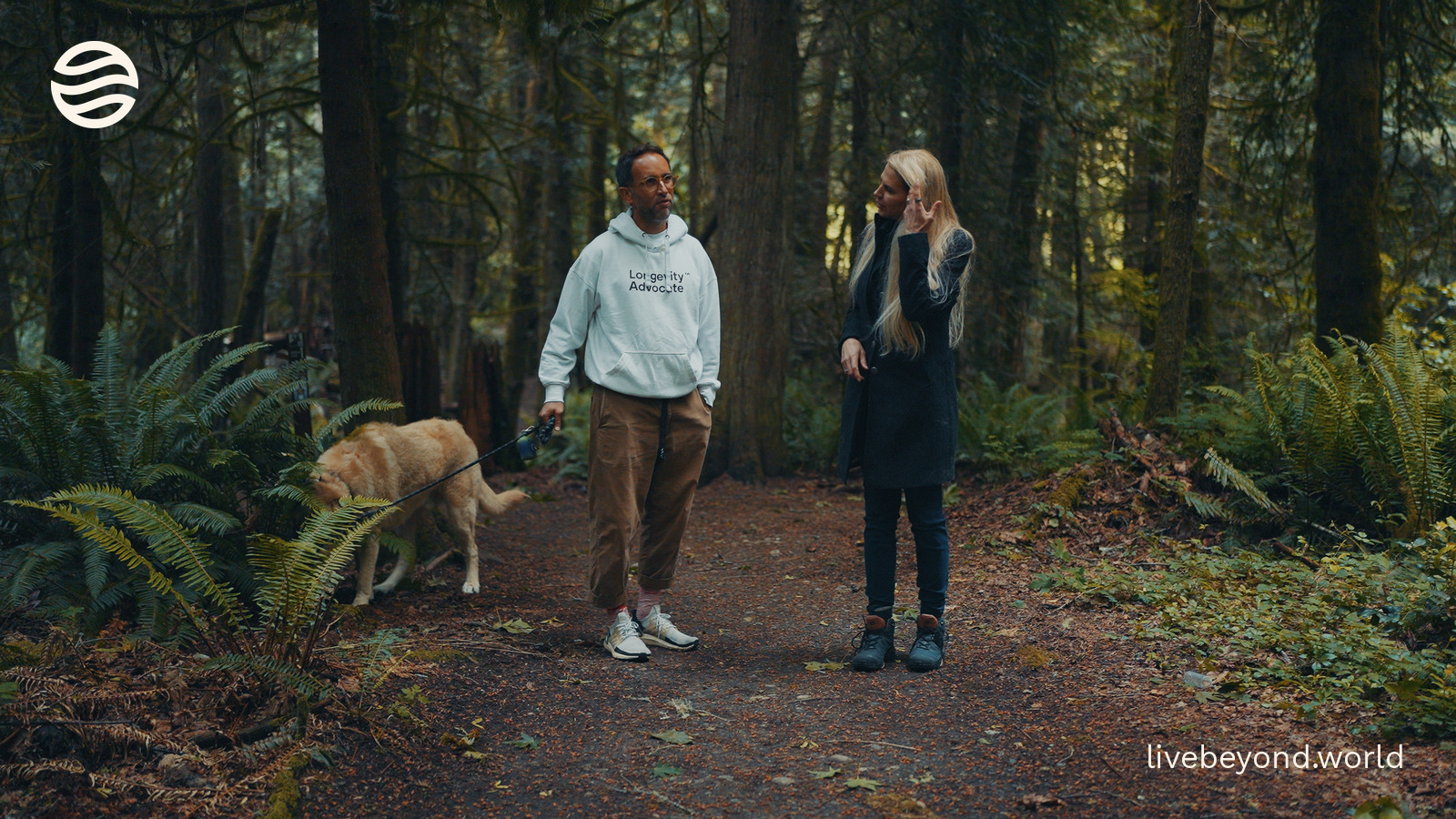 Marek and Liz Parrish walking with a dog on a path through a tall green forest.