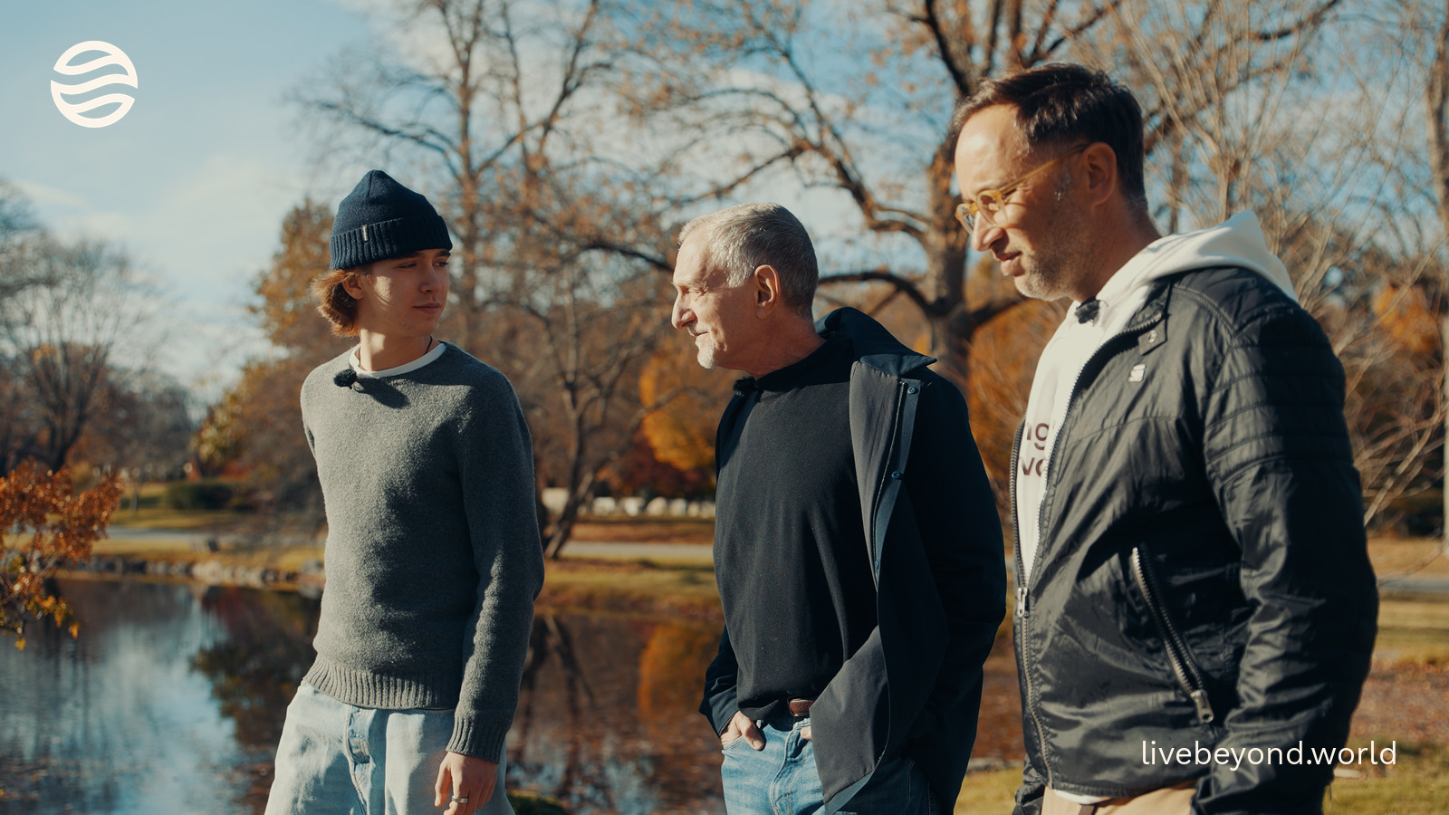 Alek, Robert Waldinger and Marek talking by a pond among autumn trees.