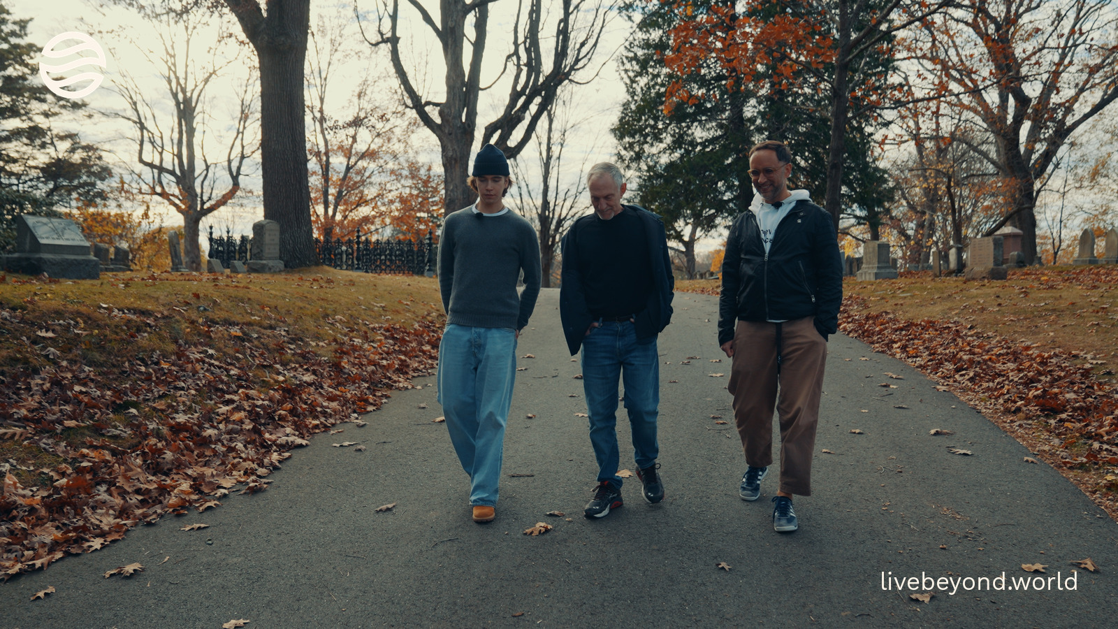 Alek, Robert Waldinger and Marek walking together along a path lined with autumn trees.
