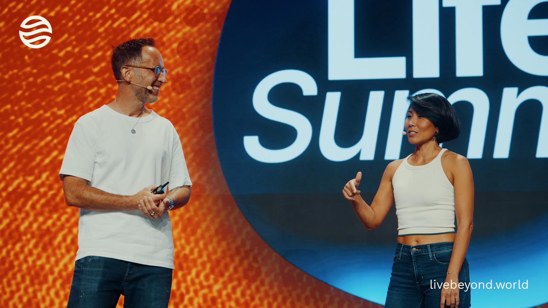 Marek smiling and Dr Olivia Lesslar speaking on stage in front of the big orange LifeSummit screen.