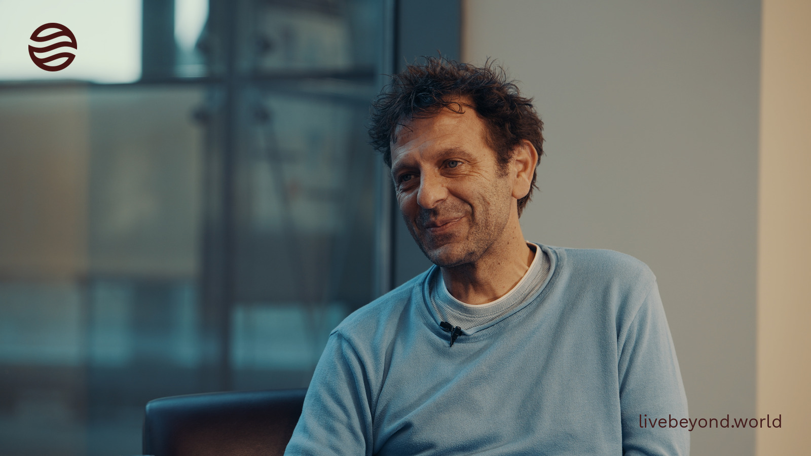 Vittorio Sebastiano smiling during our interview, in a light blue sweater by a tall window.