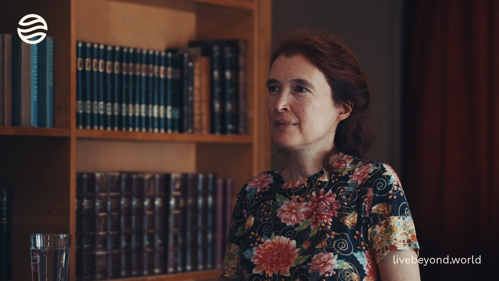 Vera Gorbunova in a floral blouse, in front of a bookcase.