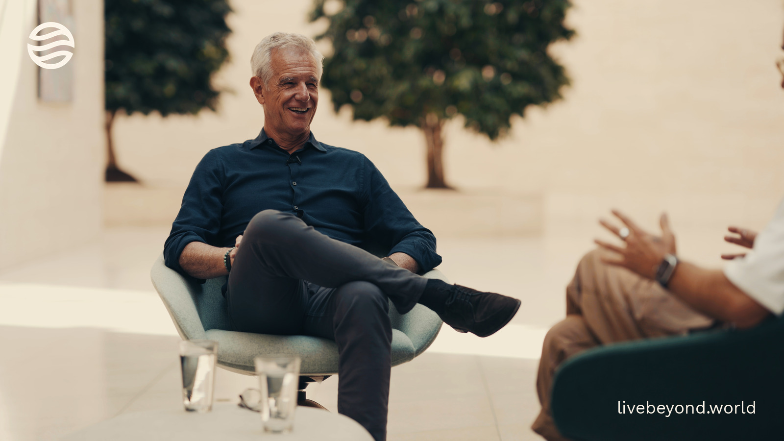 Eric Verdin sitting in an armchair in the bright atrium of the Buck Institute, talking.