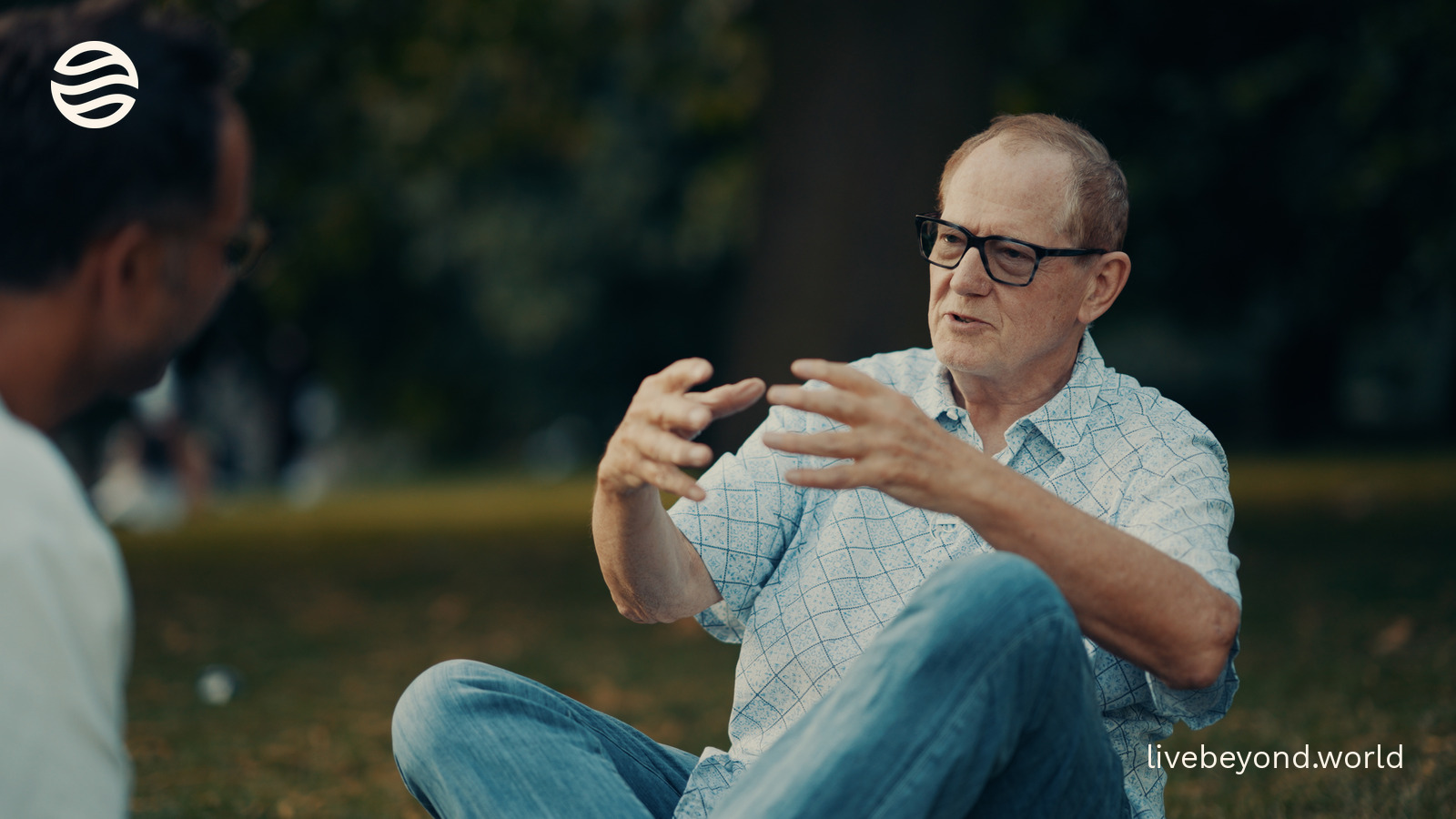 Richard Barker sitting on the grass in a London park, talking with his hands.