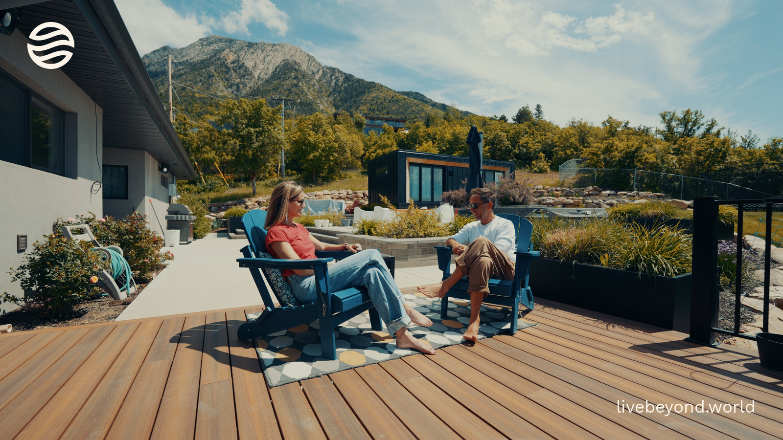 Amy Killen and Marek sitting in blue deck chairs on a terrace, mountains behind them.