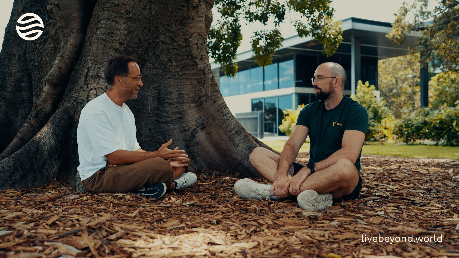 Marek and Tim Veron sitting on the ground under a huge tree, talking.