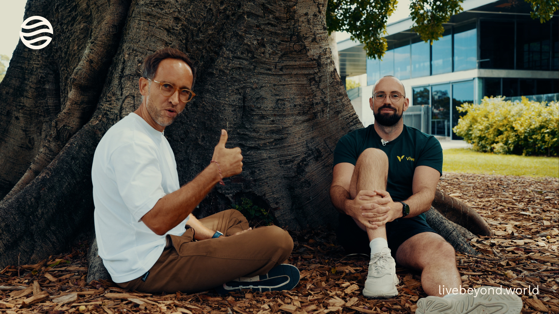 Marek giving a thumbs-up as he sits with Tim Veron at the foot of a huge tree in Sydney.