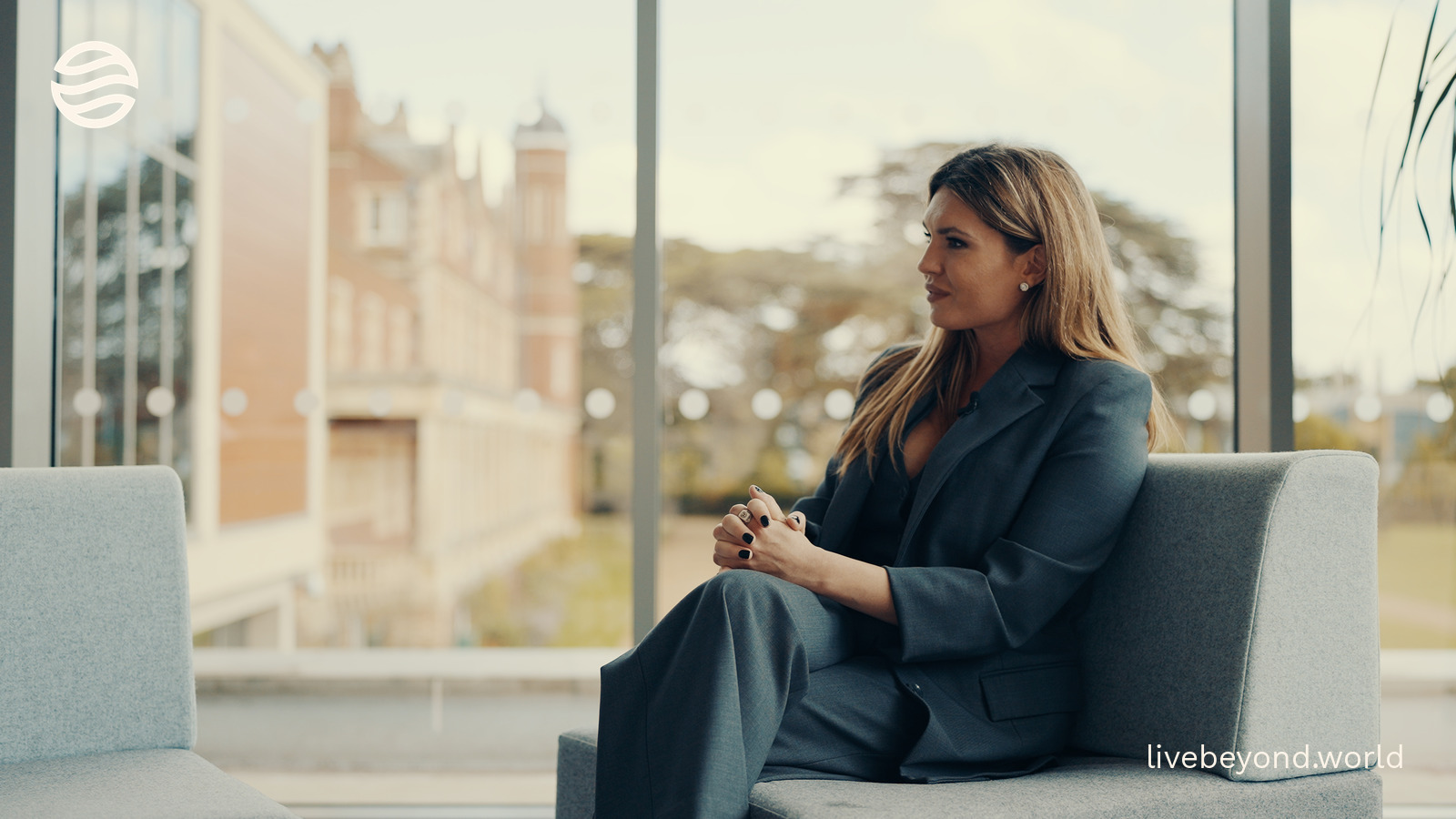 Staša Stanković sitting on a sofa by a glass wall, the old institute building behind her.