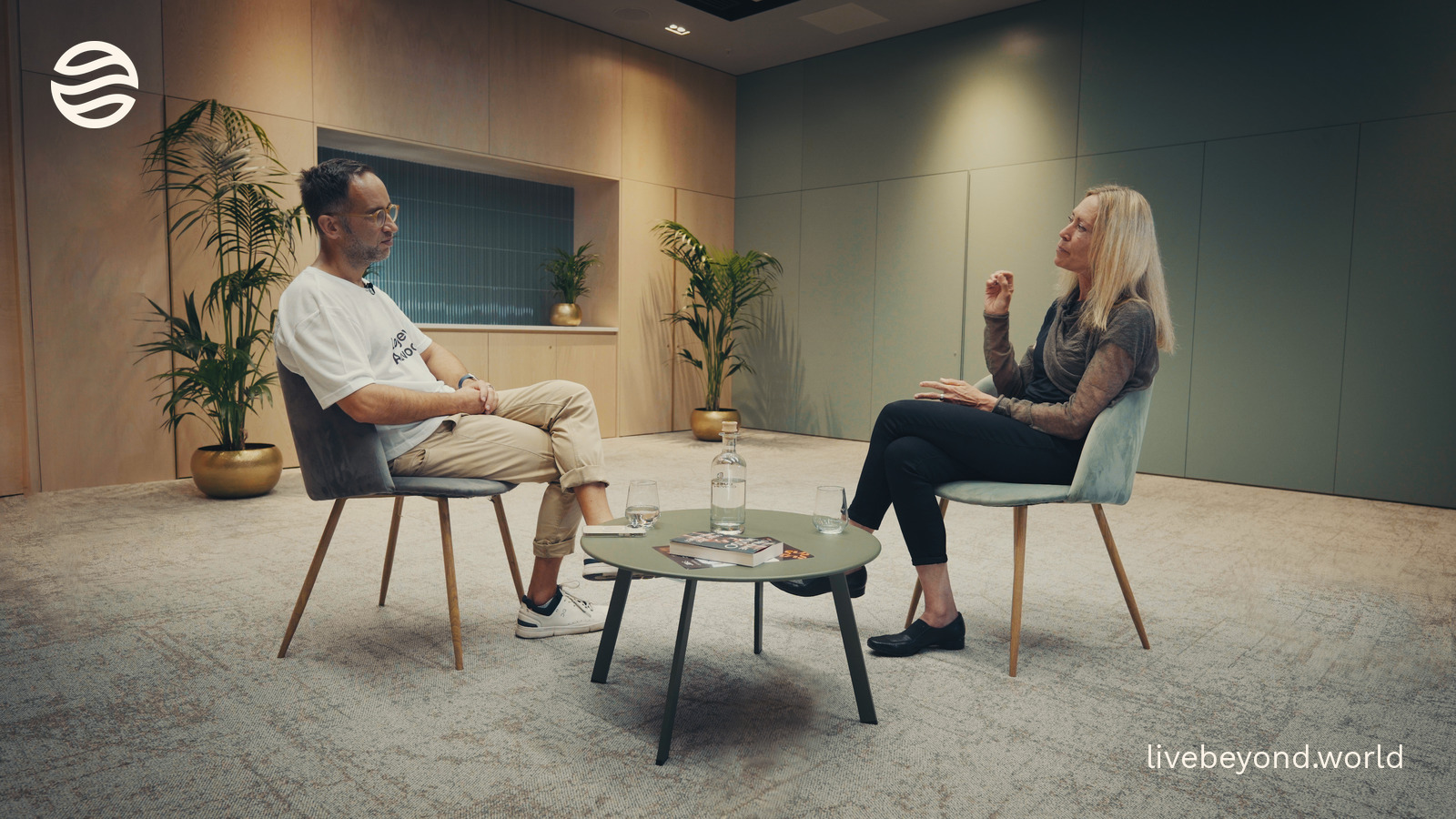 Marek and Tina Woods talking across a small table in an interview room.