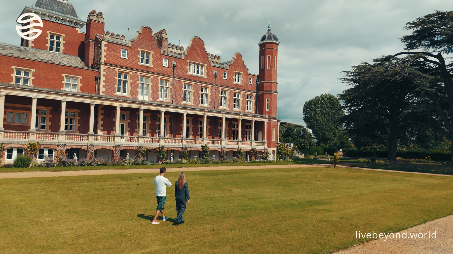 Marek and Staša Stanković walking on a wide lawn in front of the red-brick Babraham Institute building.